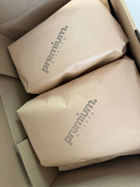 Two brown paper-wrapped packages with 'premium biltong' branding inside a cardboard box.