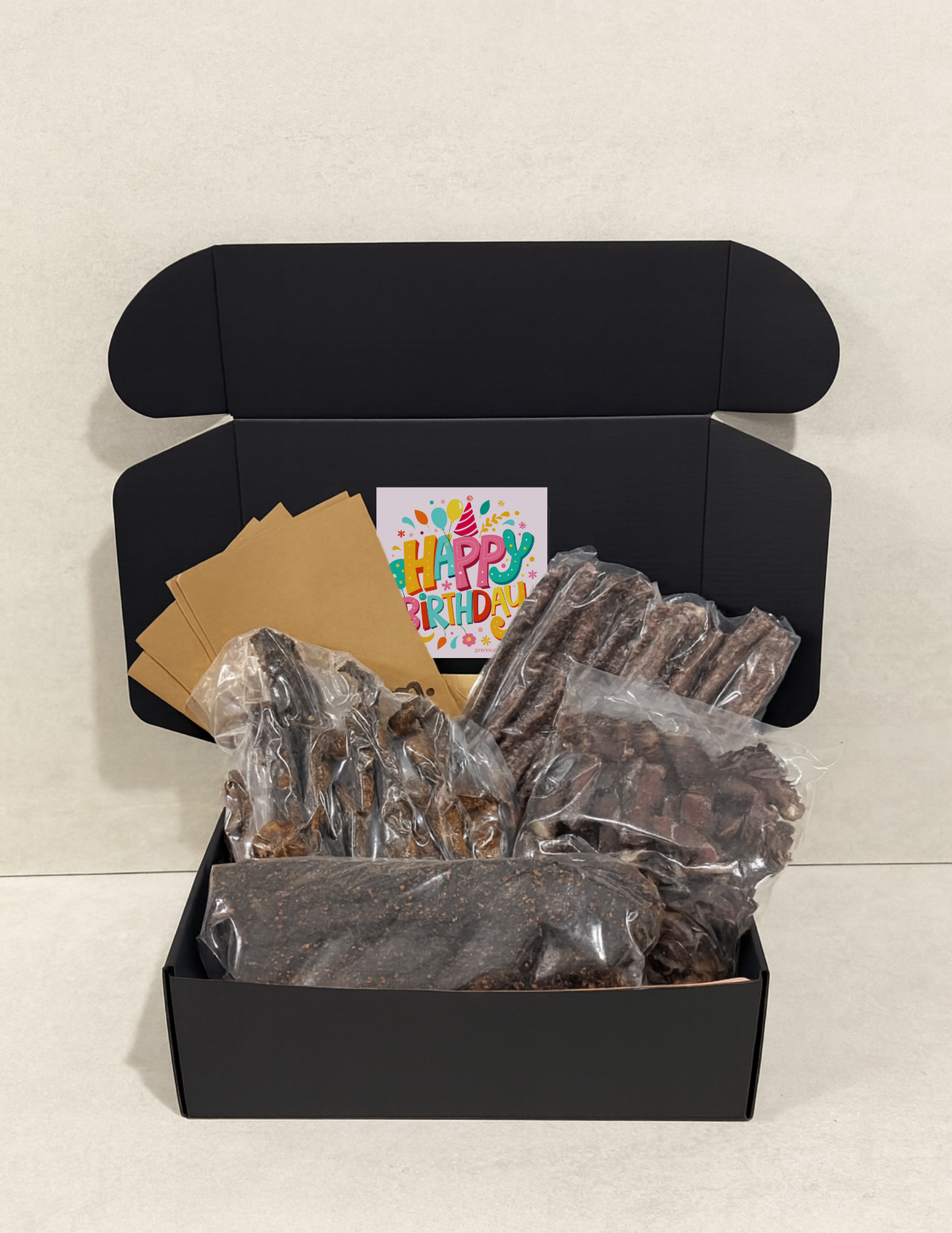 Black gift box with birthday card and wrapped biltong and droewors on a light background