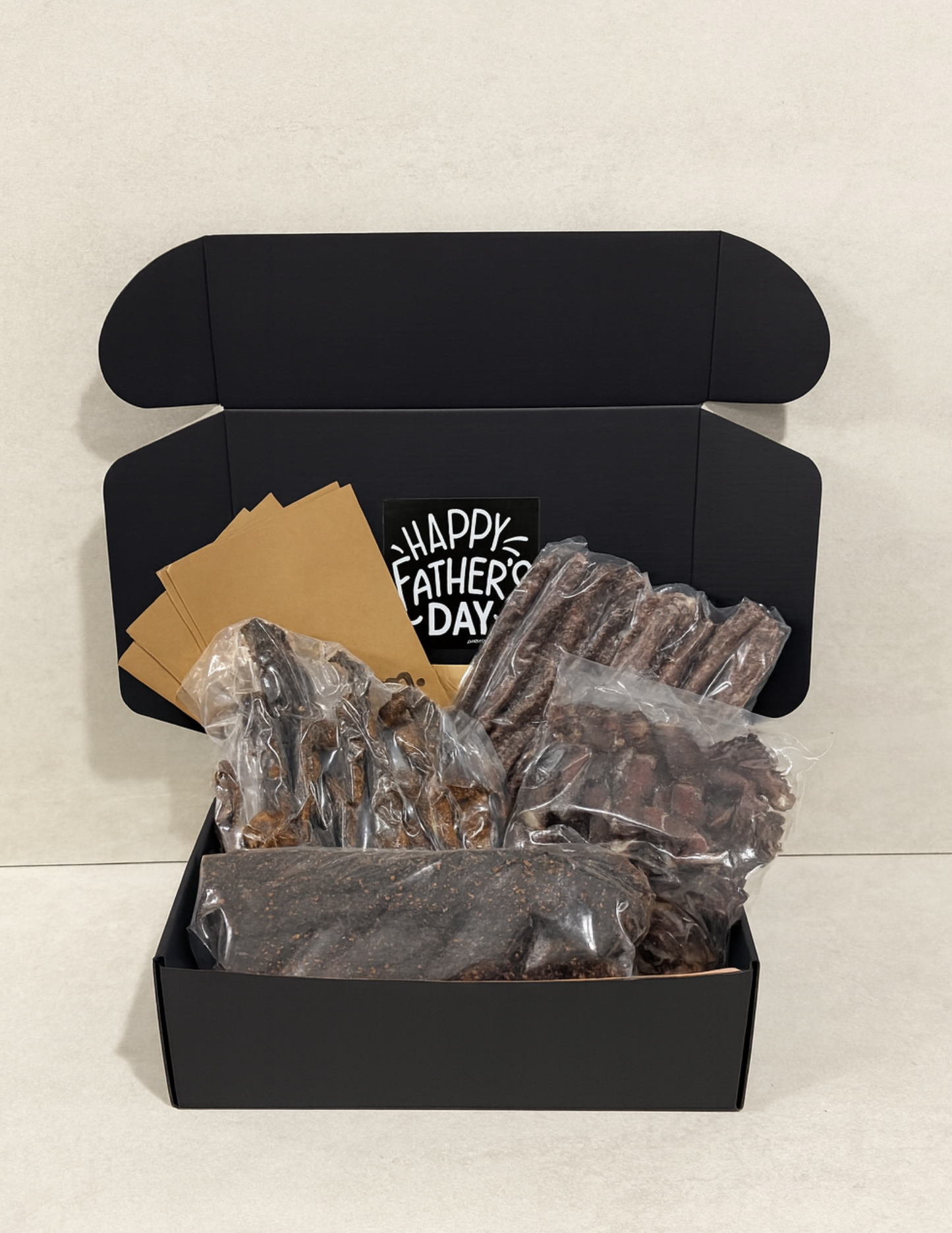 Black gift box with biltong, droewors and chilli stokkies and a 'Happy Father's Day' card on a light background
