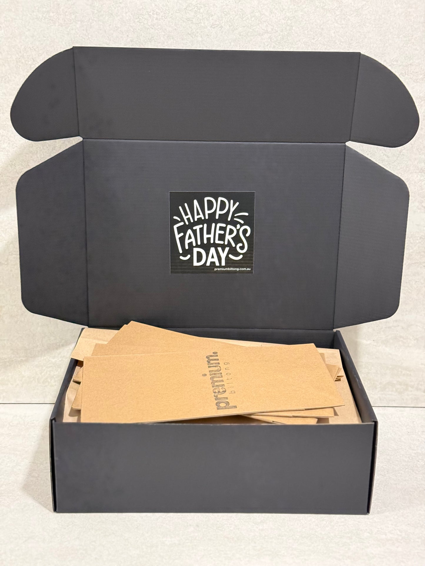 Black box with 'Happy Father's Day' card and brown envelopes on a light gray background