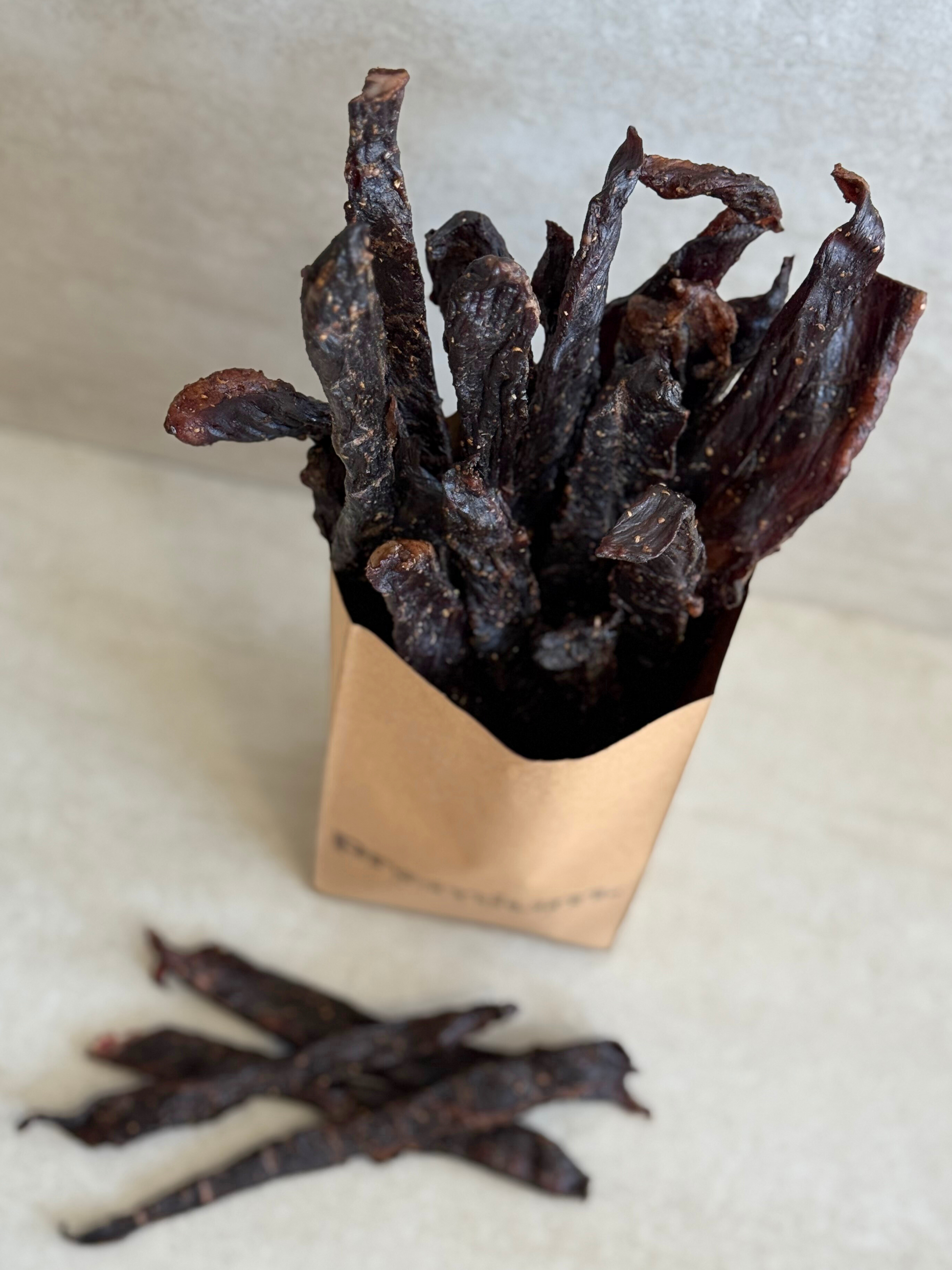Dried beef jerky sticks (stokkies) in a brown paper bag on a light background