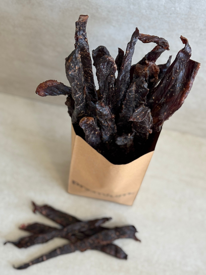 Dried beef jerky sticks (stokkies) in a brown paper bag on a light background
