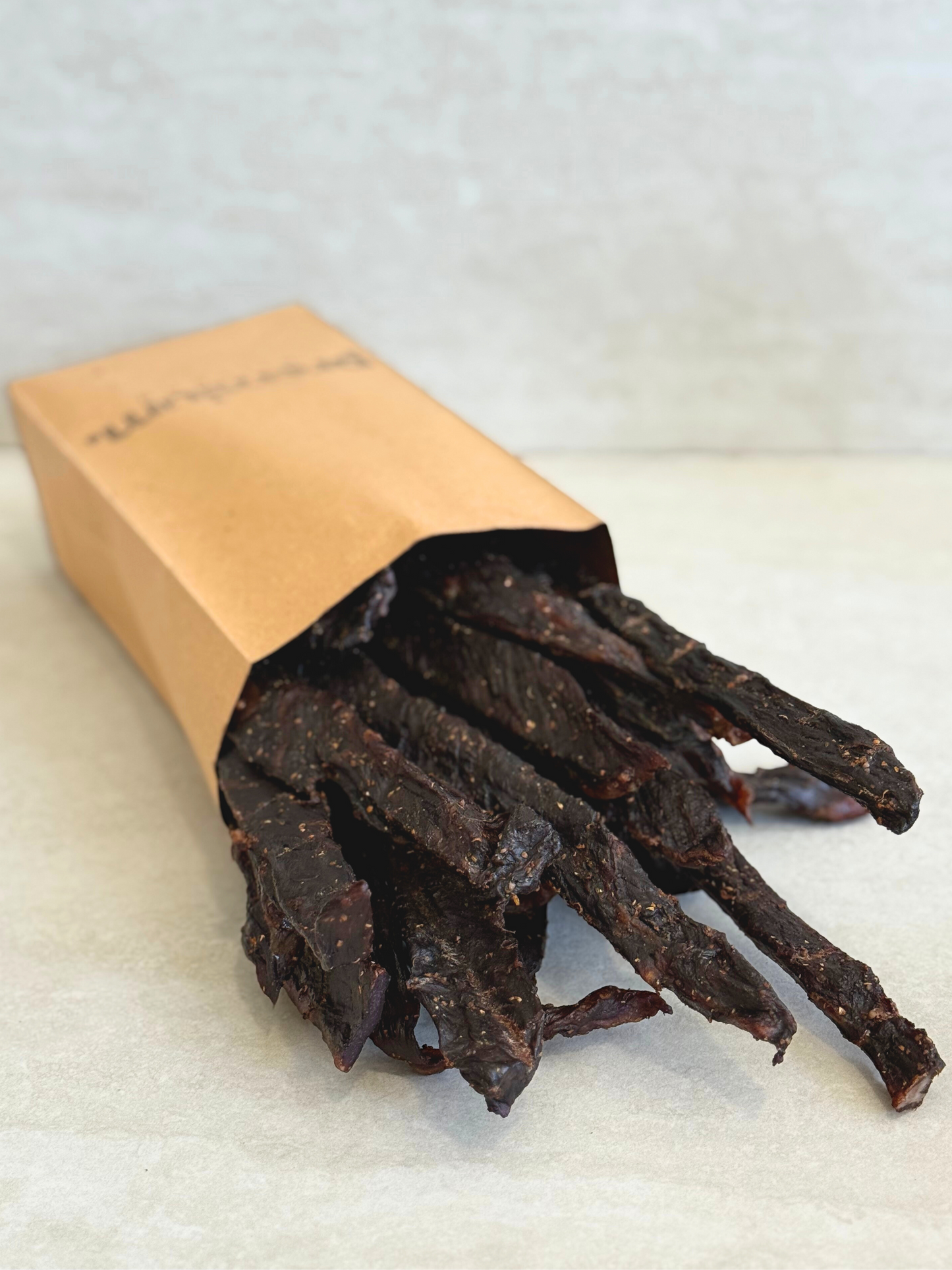 Dried meat jerky sticks stokkies in a brown paper bag on a white surface