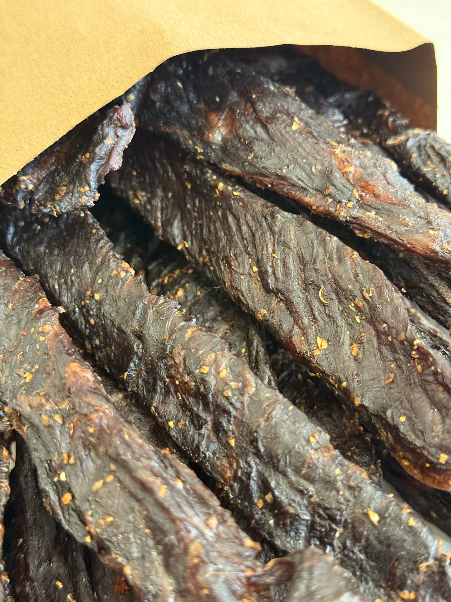 Dried beef jerky with visible seasoning in a paper bag