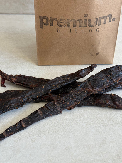 Biltong sticks next to a 'premium biltong' box on a light background