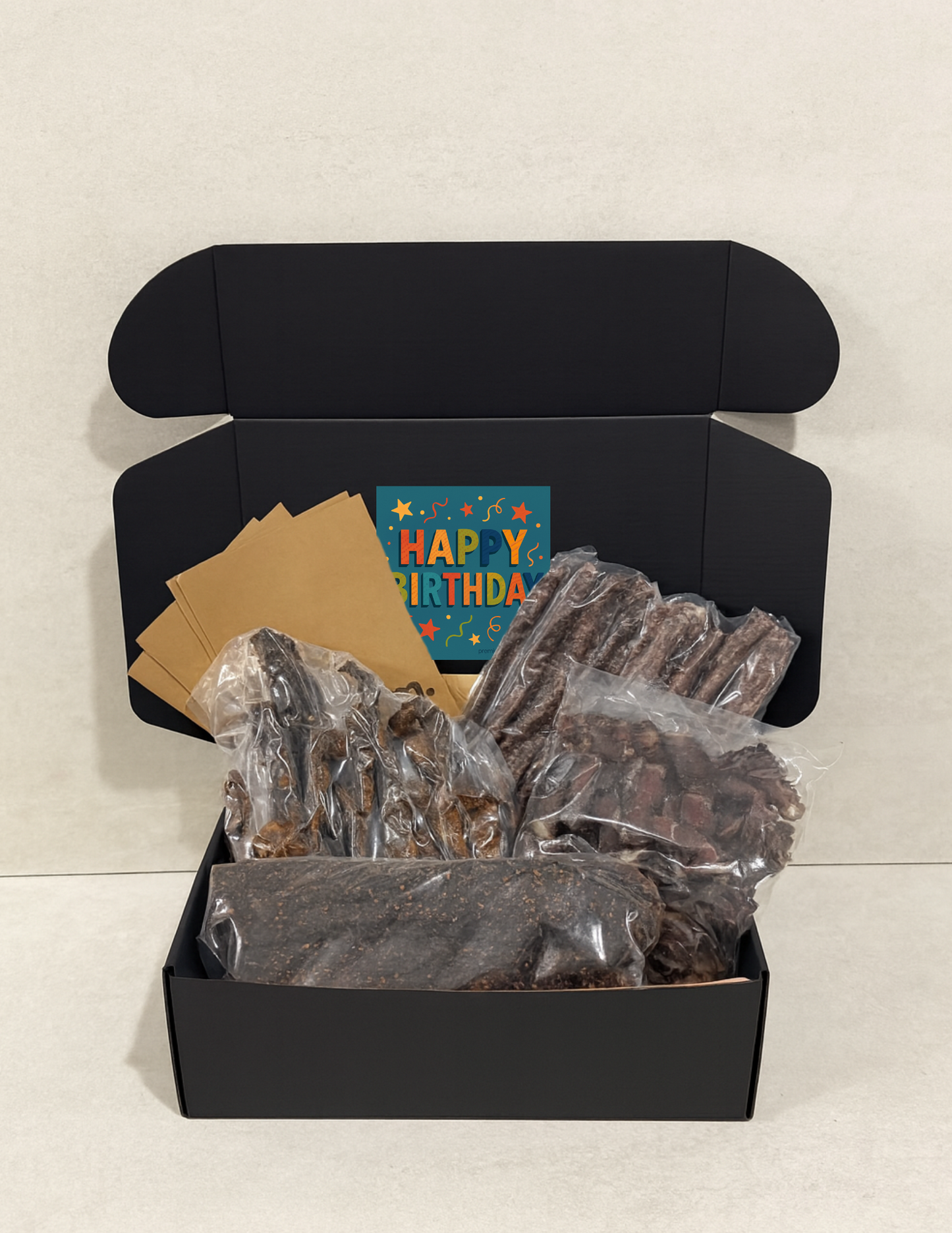 Black gift box with birthday card and wrapped biltong and droewors on a light gray background