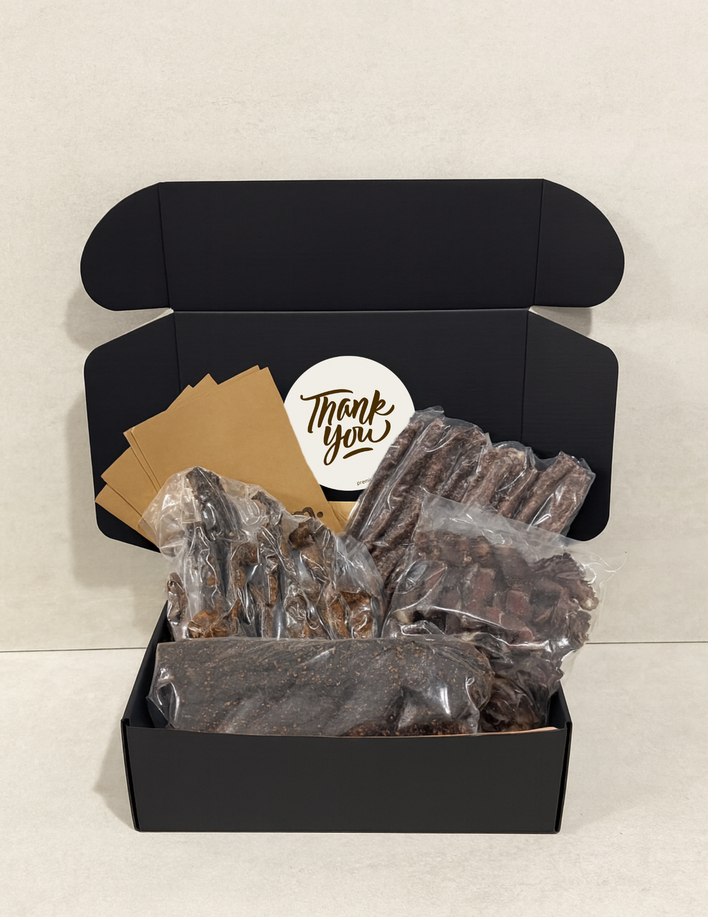 Black gift box with a 'Thank You' card and vacuum packed biltong and droewors on a light background