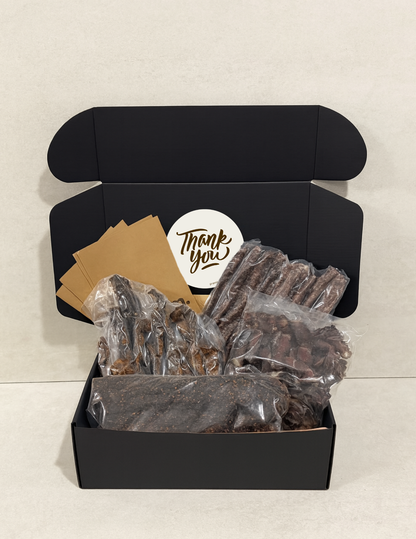 Black gift box with a 'Thank You' card and vacuum packed biltong and droewors on a light background