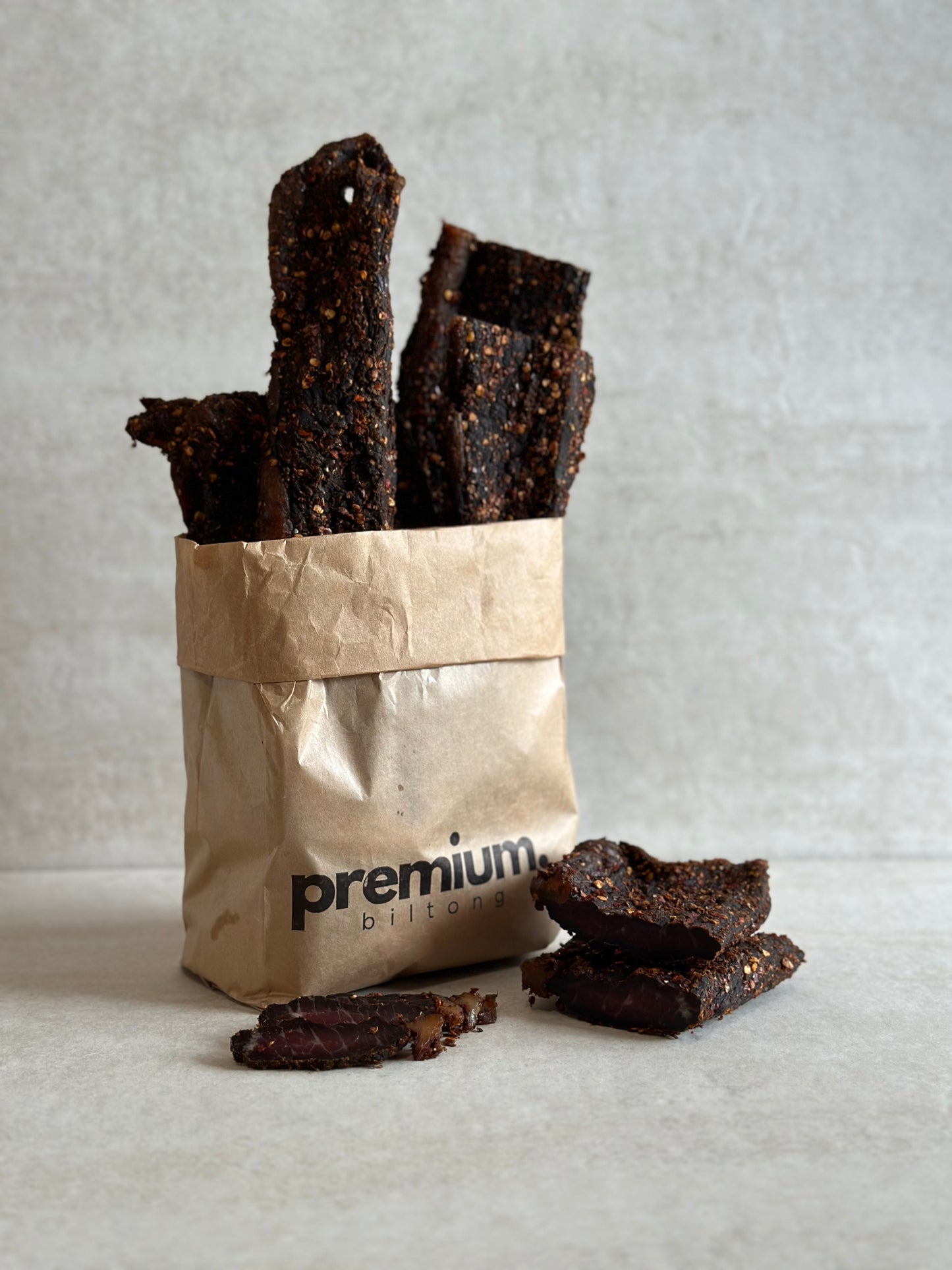A paper bag filled with whole pieces of chilli biltong, a traditional South African dried meat snack, seasoned with salt, pepper, chilli and coriander.